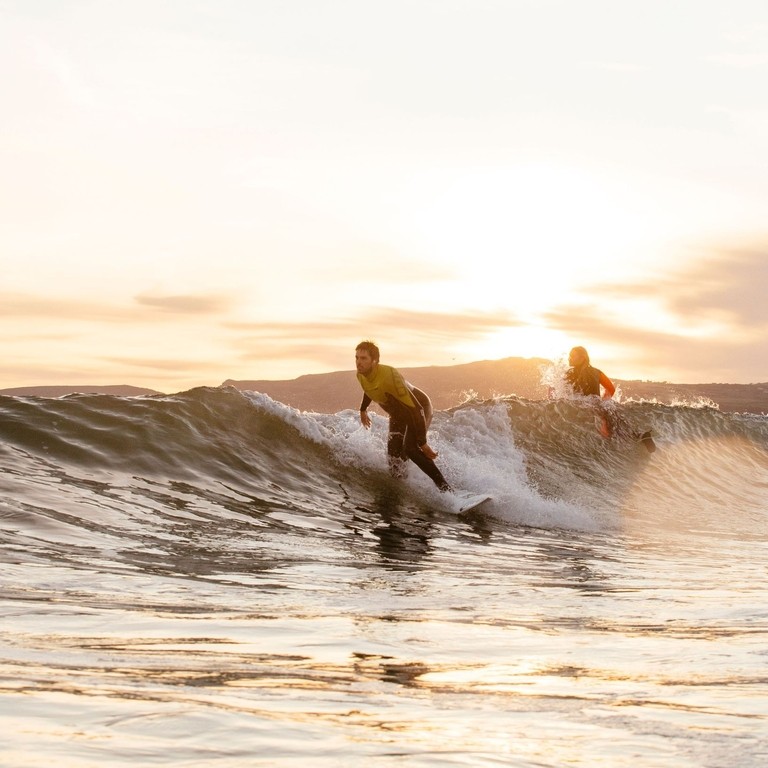 Hombre y mujer, en traje de neopreno, surfeando una pequeña ola