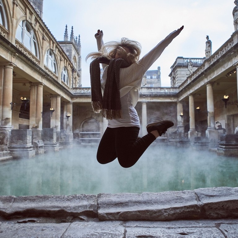 Woman leaping in the air at The Roman Baths, Bath, Somerset, England.