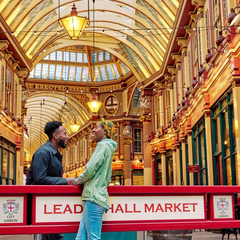 Smiling couple engaged in conversation outside a market hall with an ornate decorated gold ceiling.