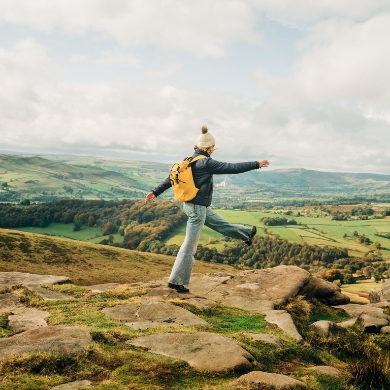 Woman skipping on rocks at edge of hill. Landscape view