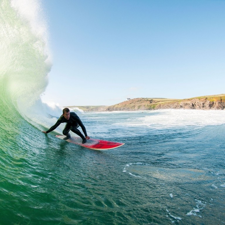 Surfista con traje de neopreno surfeando una gran ola en una tabla de surf roja