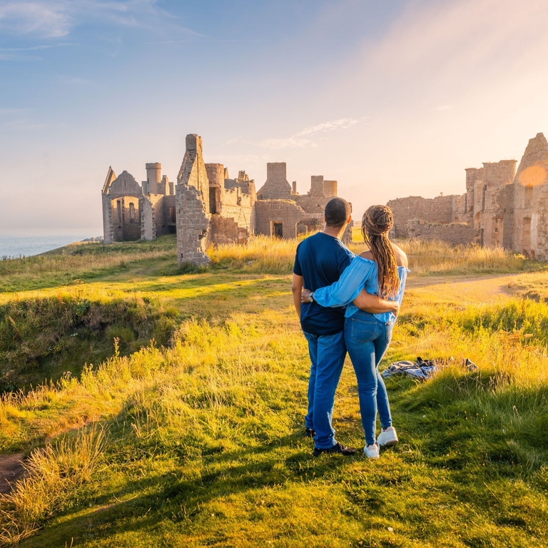 A couple enjoying the views of a castle remains at golden hour.