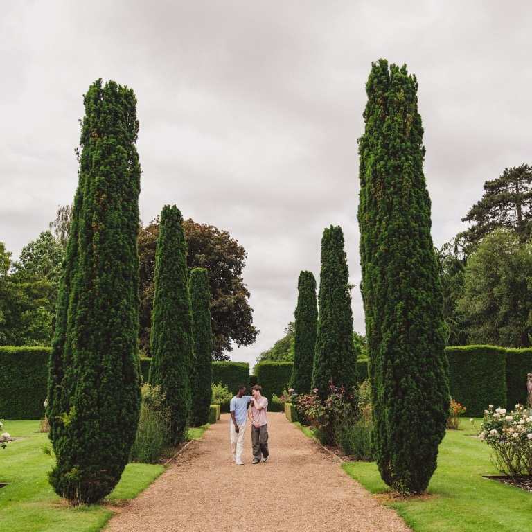Two young men walk through ornate gardens