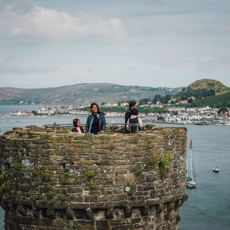 Family on top of a castle enjoying river views with boats docked and hills in the distance