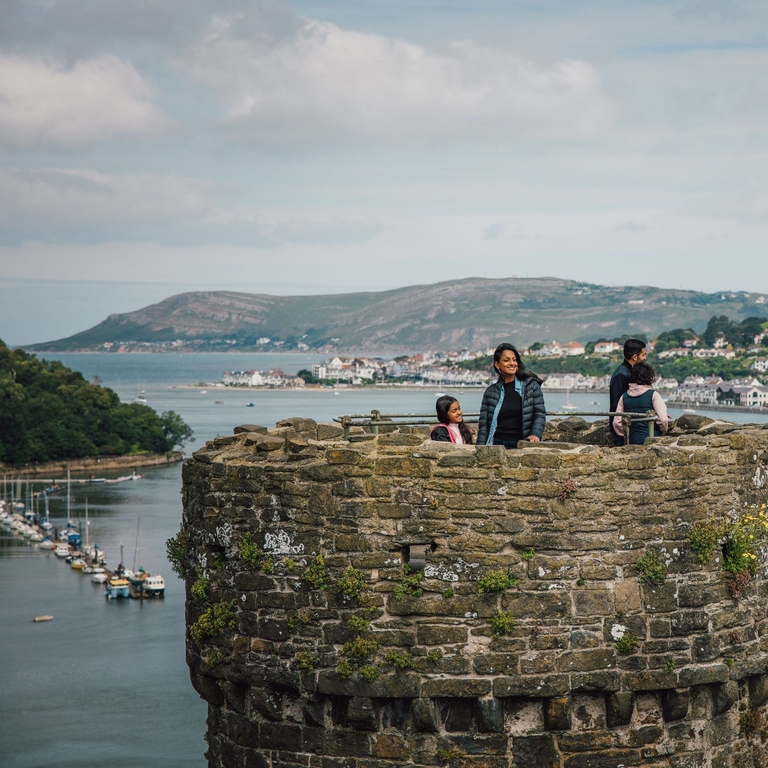 Family on top of a castle enjoying river views with boats docked and hills in the distance
