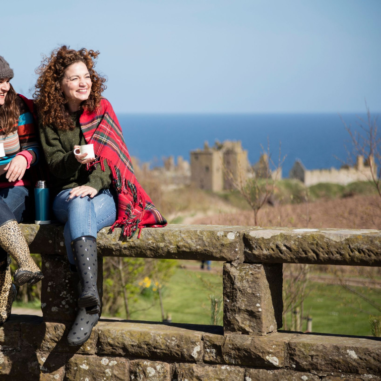 Women holding mugs with hot drinks, sitting on a stone wall