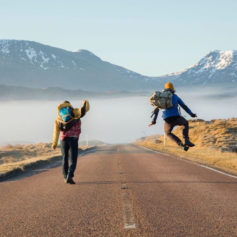 Rear view of two men jumping with joy on a country road