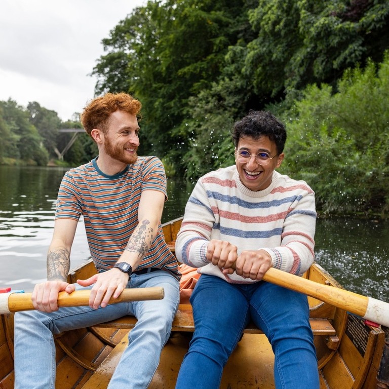 A male couple sitting in a rowboat, rowing together