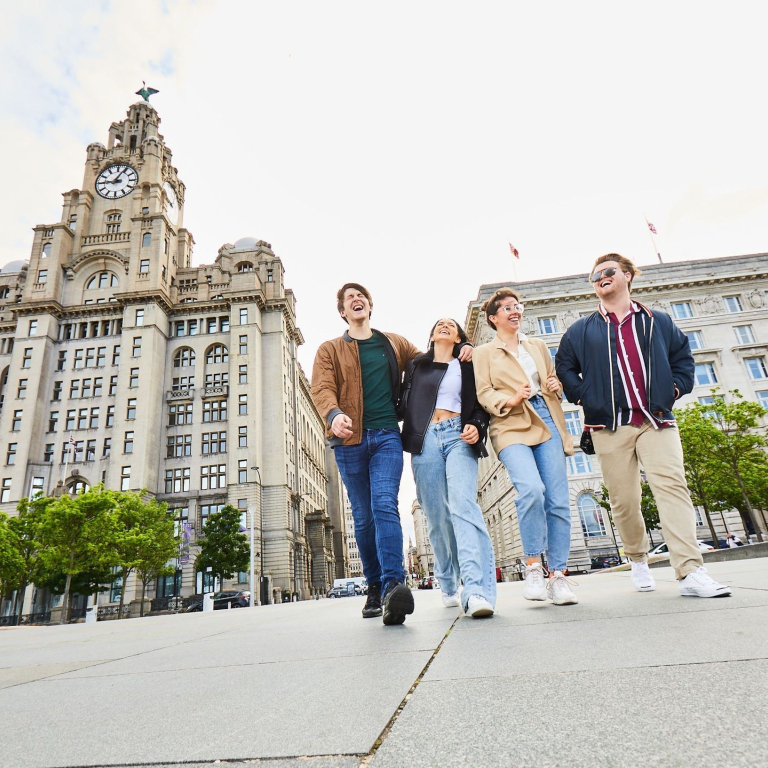 Four friends exploring a local city walking along waterfront promenade, with historic buildings in the background