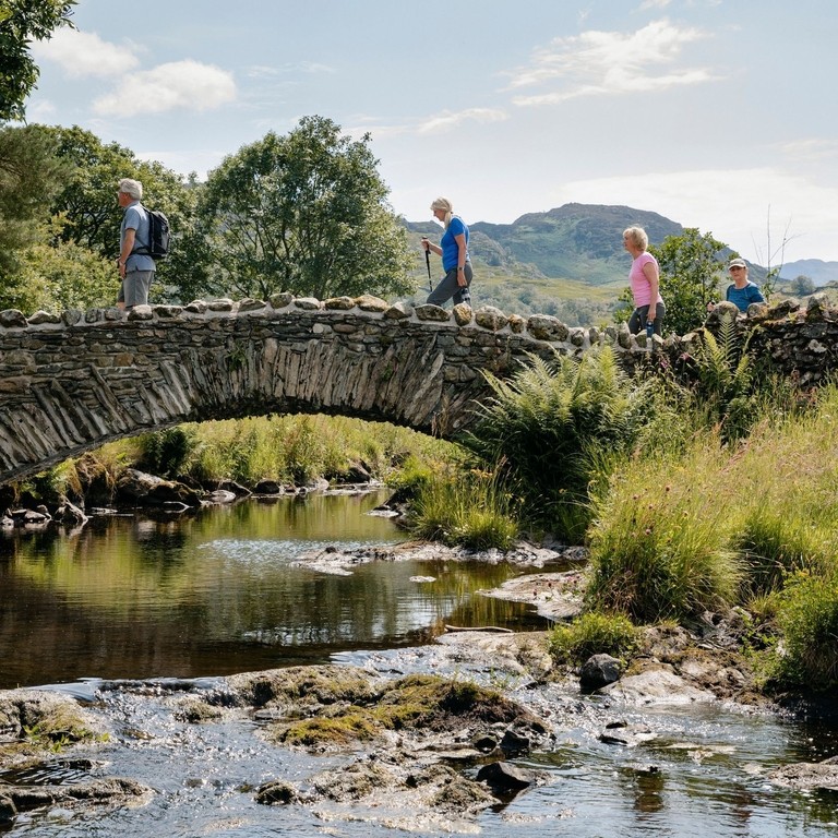 Group of friends out walking in the lakes crossing bridge in the Lake District