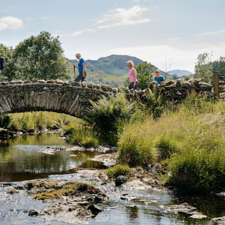 Group of friends out walking in the lakes crossing bridge in the Lake District