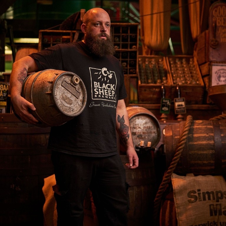 Man standing in store room, holding wooden beer barrel