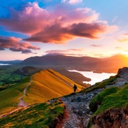 Hiker walking along a path on the mountain ridge at sunset