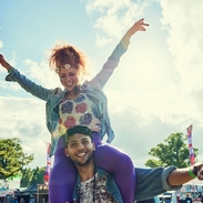 A woman sits on a mans shoulders at a festival in the summertime