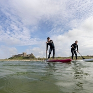 Two men on are paddleboarding in the sea with a heritage castle in the background.