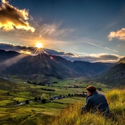 Mann sitzt im langen Gras und beobachtet den Sonnenaufgang zwischen Tälern