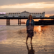 Woman standing on the beach near the pier at sunset