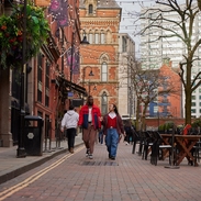 Two men chatting and walking down a street with cafes and a canal.