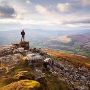 Man atop a vast colourful mountain range at sunset looking out into the valley