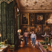 Two women walk through an ornate room in a heritage house