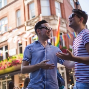 Young male gay couple talking outside a bar in the sunshine.