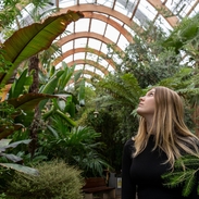A woman walking past plants in a large temperate glasshouse