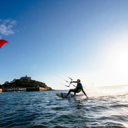 A man on a surfboard holding control bar of a kite canopy