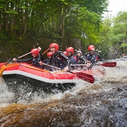 People wearing wetsuits and helmets paddling down a rapid