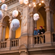 Two men looking at installation of suspended head sculptures