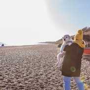 A woman carrying a dog along a beach in Dunwich