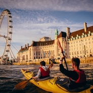 Two people kayaking on the Thames towards the London Eye