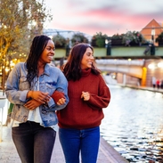 Two women, linking arms, walking beside a canal in evening
