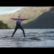 A woman stands on a paddleboard on a loch with mountains behind