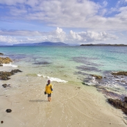 A high angle view of an independent young woman walking on the white sand with the crystal clear blue waters of Iona, Scotland