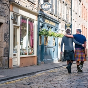 Gleichgeschlechtliches männliches Paar in Schottenröcken geht Arm in Arm