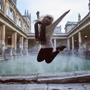 Woman leaping in the air at The Roman Baths, Bath, Somerset, England.
