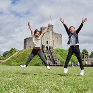 Two children jumping in front of a castle.