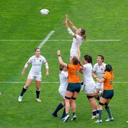 Women's rugby match with players from two teams jumping to catch the ball on the field