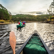 People paddling Indian canoes on water between greenery