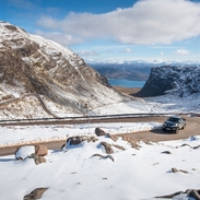 A pickup truck drives up a windy, hilly road lined with snow in winter