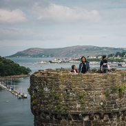 Family on top of a castle enjoying river views with boats docked and hills in the distance