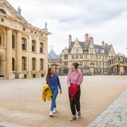 Two women walk across a courtyard among heritage buildings