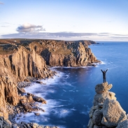 Man standing on a rocky peak on the edge of the coast looking over the headland