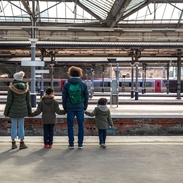 A multiracial family of four, a mother, father and their two little boys standing Newcastle railway station platform waiting for their train.