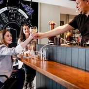 Two women, one in a wheelchair being served a drink by a bartender in a distillery bar