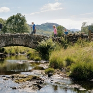Group of friends out walking in the lakes crossing bridge in the Lake District