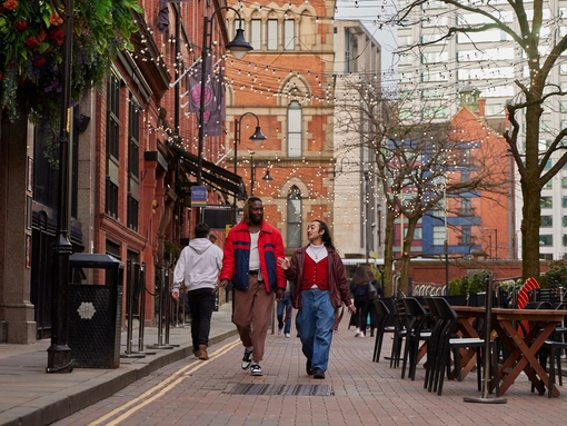 Two men chatting and walking down a street with cafes and a canal.