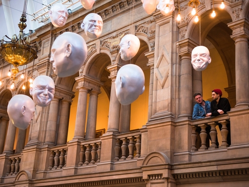 Two men looking at installation of suspended head sculptures