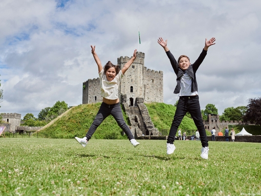 Two children jumping in front of a castle.