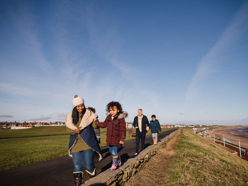 Family and friends walking along a coastal path in the winter sunshine